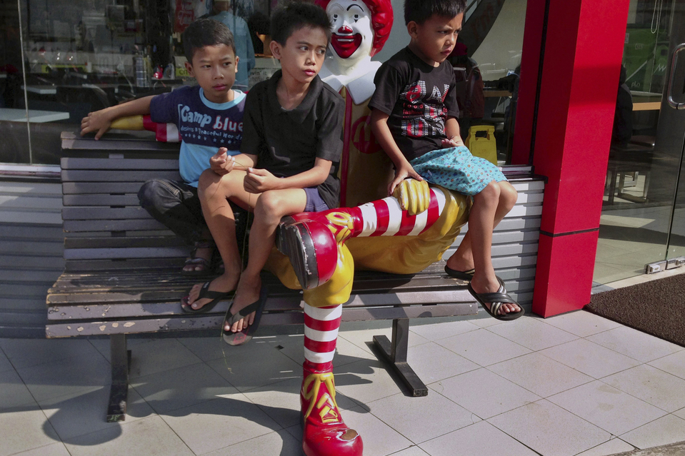 Trẻ em ngồi trên bức tượng Ronald McDonald bên ngoài một nhà hàng ở Bandung, Indonesia.