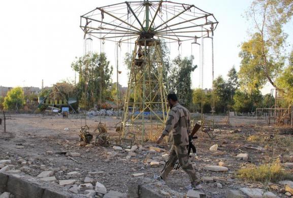 Một chiến binh của lực lượng quân đội Syria tự do đi qua một công viên giải trí bị phá hủy ở thành phố Deir al-Zor, Syria.