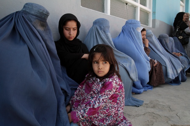 Một bé gái ngồi cạnh mẹ xếp hàng chờ nhận thực phẩm miễn phí từ một tổ chức phi chính phủ ở Kabul, Afghanistan.