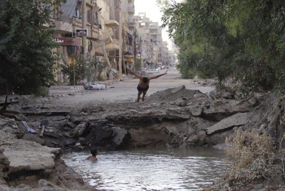 Các cậu bé tắm dưới hố đầy nước trên đường phố do đạn pháo tạo ra ở Deir al-Zor, Syria.