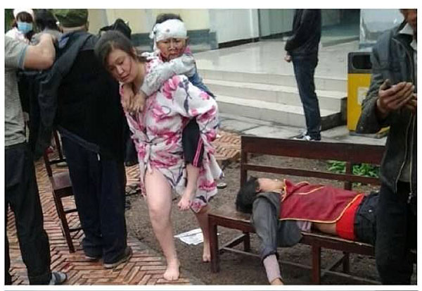 Một nạn nhân bị thương nằm trên ghế chờ được chăm sóc, trong khi một phụ nữ cõng em bé bị thương sau khi được sở cứu.