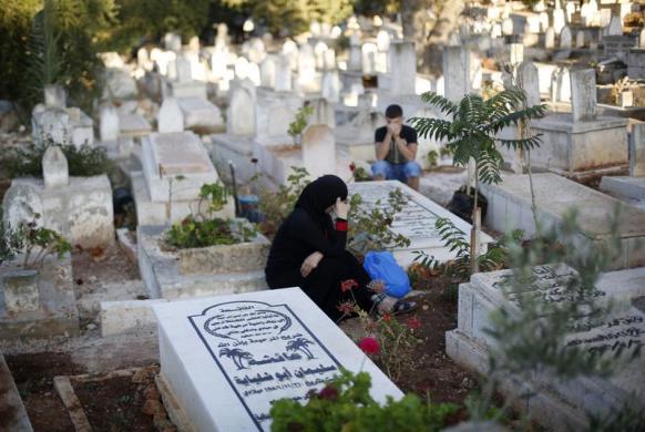 Người Palestin ngồi cầu nguyện cạnh mộ của người thân trong dịp lễ Eid al-Fitr tại một nghĩa trang ở Bờ Tây.