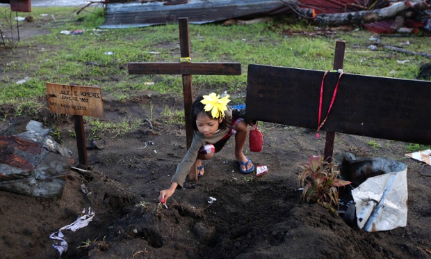 Bé gái Jaysel Mosquito, 6 tuổi, cắm kẹo lên mộ 4 thành viên gia đình thiệt mạng trong siêu bão Haiyan ngoài nhà thờ San Joaquin ở Palo, Philippines.