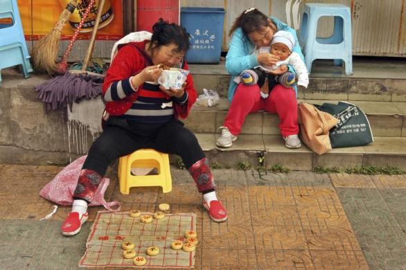 Một phụ nữ ăn mì tôm trong khi chờ khách tới giải cờ thế trên đường phố ở Quý Dương, Trung Quốc.