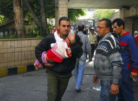 Một người đàn ông bế em bé bị thương sau vụ đánh bom trước nhà ga tàu hỏa al-Hejaz ở Damascus, Syria.