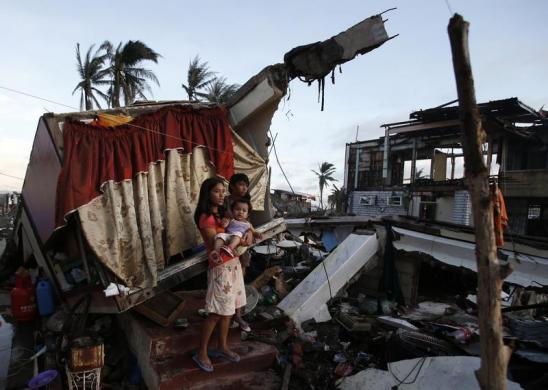 Mọi người đứng tại lối vào một căn nhà bị tốc mái tại thành phố Tacloban, Philippines.