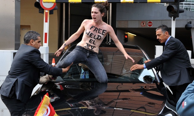 Nhân viên an túm chân một người đẹp ngực trần thuộc nhóm Femen đang ngồi trên kính chắn gió của chiếc xe chở Thủ tướng Tunisia, Ali Laarayedh, khi ông đang rời khỏi trụ sở của Ủy ban châu Âu ở Brussels, Bỉ.