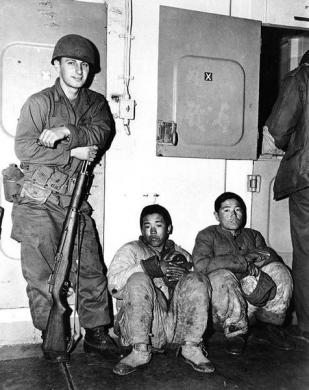 Binh lính Mỹ đứng canh hai đối tượng vừa bị bắt giữ vì vận chuyển hàng từ Hungnam tới Pusan hồi tháng 12 năm 1950