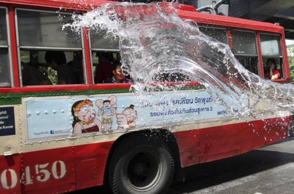 Một cậu bé hất nước lên xe bus đi qua nhà.