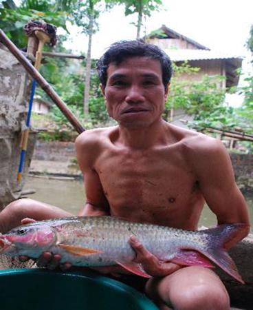 Chủ tịch xã Hà Công Sang và con cá rầm xanh trong ao nhà. Ảnh: Nông nghiệp Việt Nam