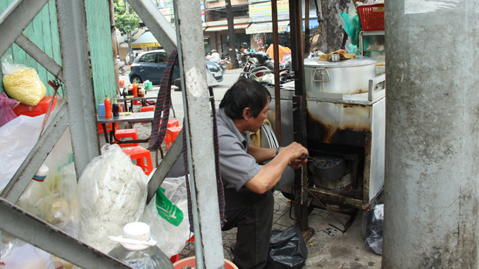 
	Ông Lương Tấn Túc (53 tuổi, quê Quảng Ngãi) bỏ than vào lò đốt để giữ
	nóng cho nồi nước lèo, phía sau là dãy bàn ghế vắng khách - Ảnh: Hữu
	Khoa