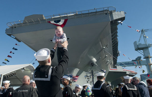 Thủy thủ Justin Greathouse bế con gái đứng gần tàu sân bay Gerald R. Ford (CVN 78) được trang hoàng nổi bật trước lễ hạ thủy.