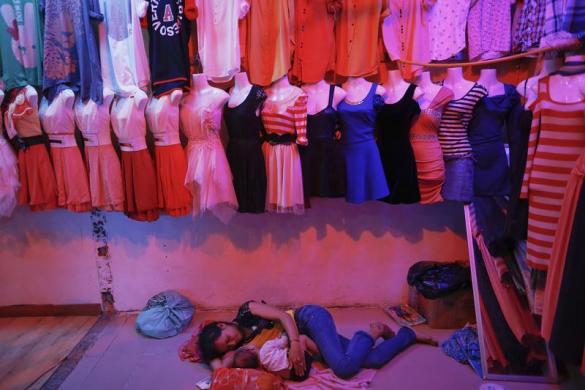 Một phụ nữ nằm ôm con trên sàn của một ki-ốt bán quần áo trong một khu chợ ở khu vực ngoại ô thủ đô Phnom Penh, Cam-pu-chia.