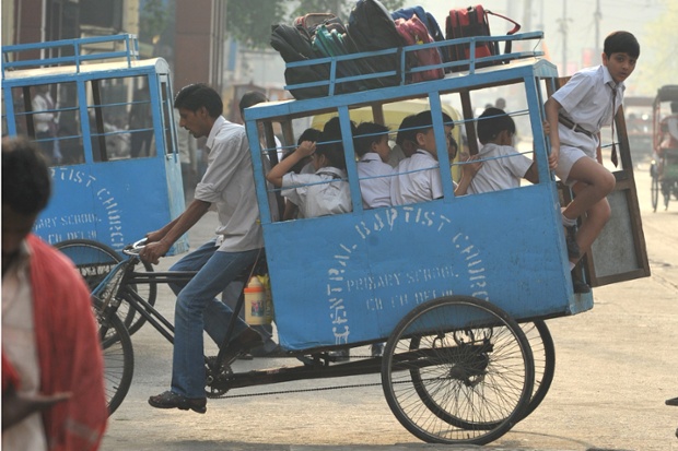 Một cậu bé xuống xe ba bánh chuyên chở học sinh tới trường ở New Delhi, Ấn Độ.