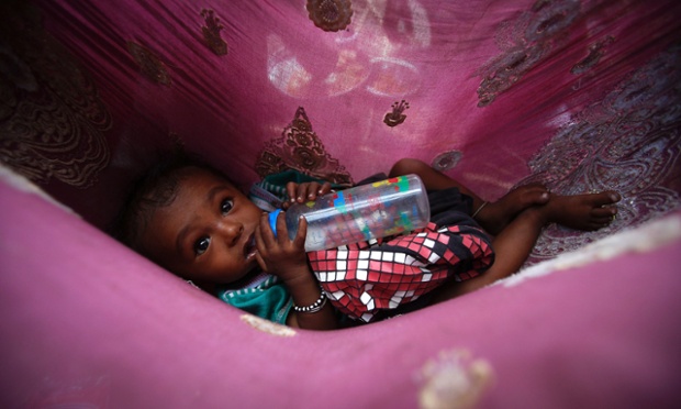 Một cậu bé vô gia cư 6 tháng tuổi nằm uống sữa bình trong một cũi nhỏ trên đường phố ở Mumbai, Ấn Độ.