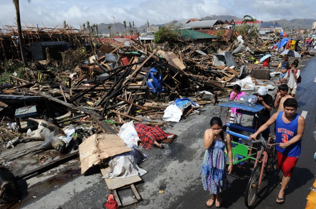 Người sống sót đi qua những ngôi nhà bị tàn phá và xác chết trên đường sau siêu bão Haiyan ở thành phố Tacloban, Philippines.