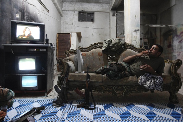Một chiến binh của lực lượng quân đội Syria tự do nằm nghỉ ngơi trên ghế sofa, xem tivi và các màn hình giám sát trong một căn phòng ở thành phố Aleppo, Syria.