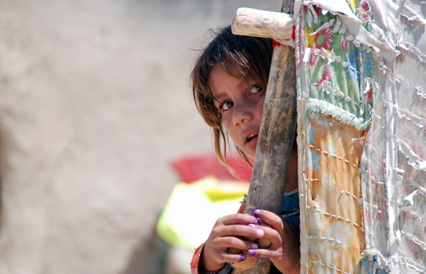 Một bé gái sống du cư nhìn ra ngoài từ túp lều tạm ở e-Sharif, Afghanistan.