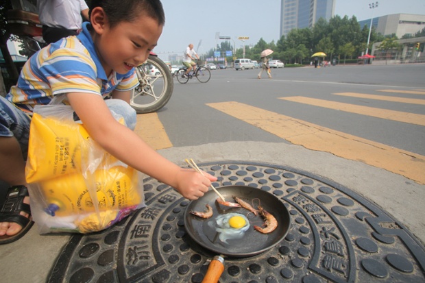Một cậu bé rán trứng và tôm trên một nắp hố gas bằng kim loại ở thành phố Tân An, Trung Quốc, khi nhiệt độ ở đây đang ở mức kỷ lục trong nhiều thập kỷ.