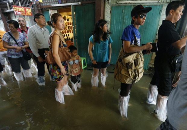 Du khách dùng túi bóng bọc chân để tránh bị ướt trong khi họ đứng chờ thuyền trên đường phố ngập nước ở Bangkok, Thái Lan.