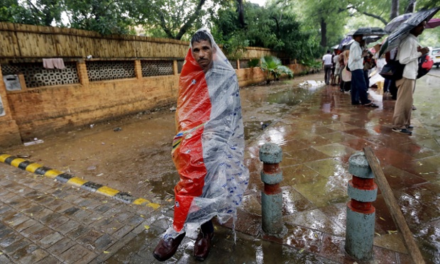 Người đàn ông mặc áo mưa ngồi chờ xe bus tại thành phố New Delhi, Ấn Độ.
