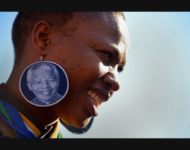 Một phụ nữ đeo khuyên tai có hình nhà lãnh đạo Nelson Mandela cùng những người khác cầu nguyện cho ông bên ngoài bệnh viện Pretoria, Nam Phi.