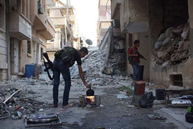 Một chiến binh của lực lượng quân đội Syria tự do đang đun nước pha trà, trong khi một đồng đội kiểm tra bên trong tòa nhà đổ nát ở thành phố Deir al-Zor, Syria.
