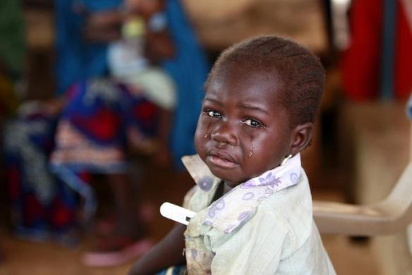 Một em bé với nhiệt kế ở nách khóc khi được bác sĩ khám tại ngôi làng Bagega, bang Zamfara, Nigeria.