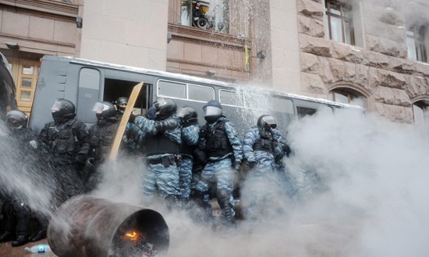 Cảnh sát chống bạo động nấp sau một chiếc xe bus khi người biểu tình phun nước vào họ tại Kiev, Ukraine.