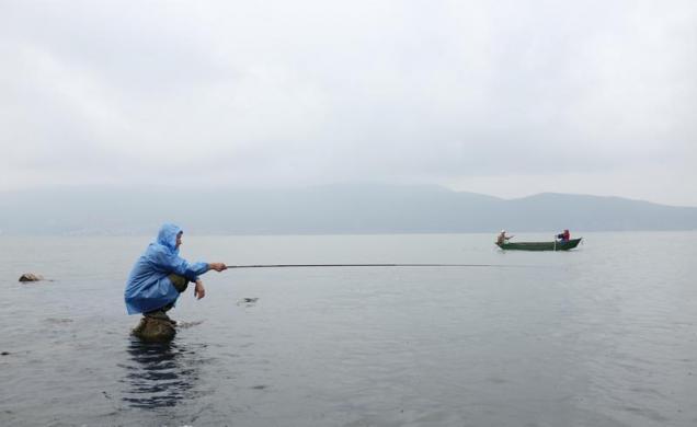 Một người đàn ông ngồi câu cá dưới trời mưa trên hồ Erhai ở thành phố Đại Lý, Vân Nam, Trung Quốc.