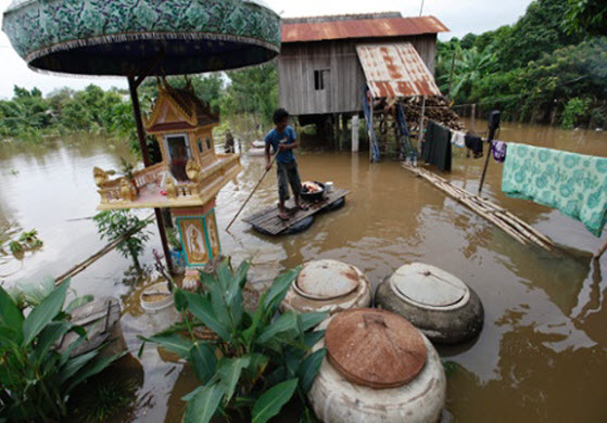 Một người đàn ông dùng bè tự chế di chuyển trên nước lũ bao quanh nhà tại một ngôi làng ở tỉnh Kandal, Campuchia.