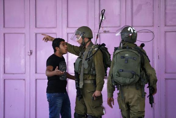 Một người Palestin cãi nhau với các binh sĩ Israel tại khu vực hạn chế đi lại ở Bờ Tây.