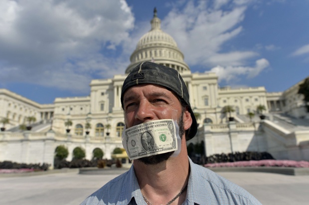 Một người biểu tình dán tờ đô la lên miệng đứng trước tòa nhà quốc hội ở Washington để yêu cầu Nghị viện Mỹ thông qua dự luật ngân sách.