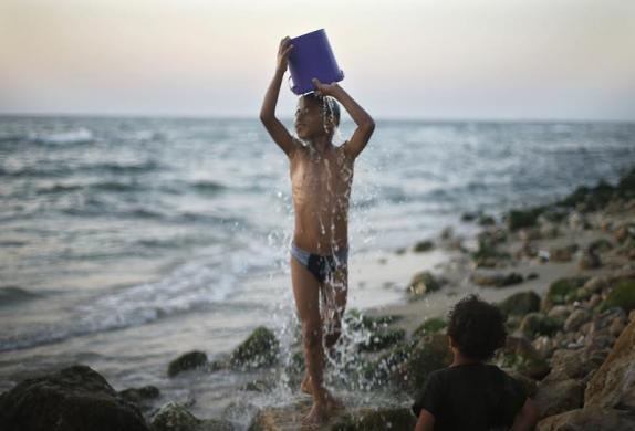 Một cậu bé người Palestin dội nước lên đầu trên bãi biển ở thành phố Gaza.