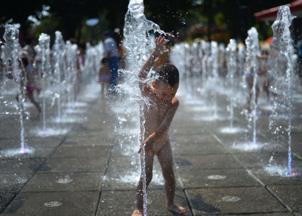 Bé trai thích thú tắm trong đài phun nước dưới trời nắng nóng ở Bucharest, Romania.