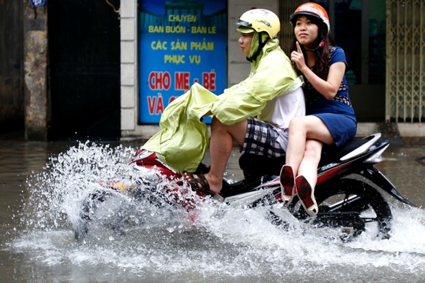 Một cặp đôi đi xe máy trên đường phố ngập lụt do mưa lớn ở Hà Nội, Việt Nam.