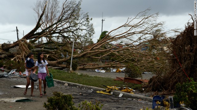 Những người phụ nữ đi qua cây đổ và nhà bị phá hủy ở Tacloban.