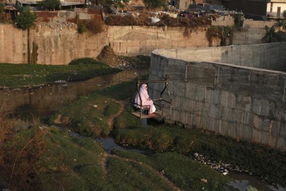 Một phụ nữ di chuyển qua một con kênh ô nhiễm bằng dây cáp ở ngoại ô Islamabad, Pakistan.