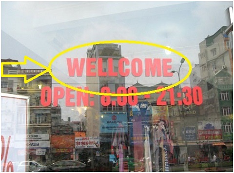 
	Tấm cửa kính sáng choang với lời chào bằng tiếng Anh viết sai chính tả "Wellcome" thay vì "Welcome".