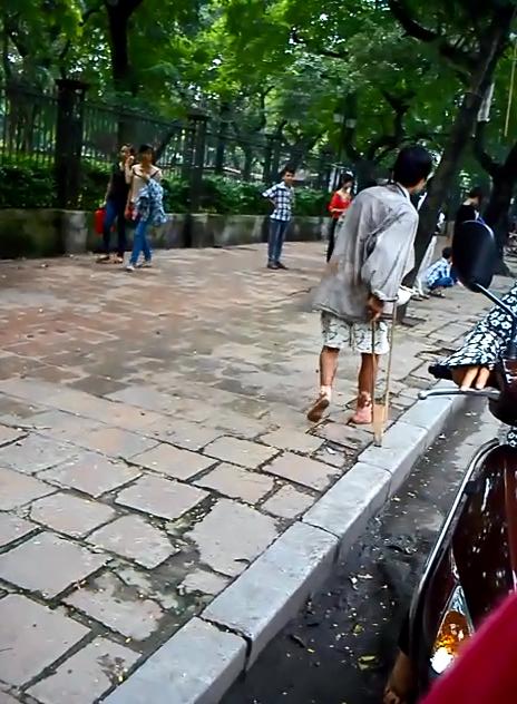 Gã ăn mày lê chân với chiếc nạng và đôi chân lở loét cùng vẻ mặt tội nghiệp để xin tiền người đi đường và du khách nước ngoài tại ngã tư Văn Miếu. (ảnh chụp sáng nay 31/5).