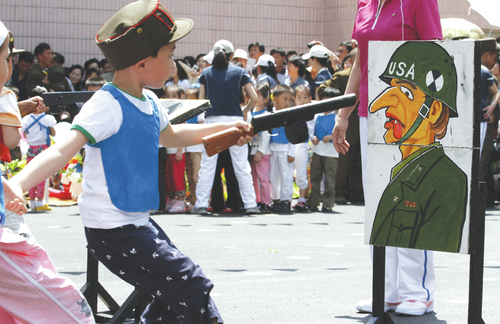 	Một đứa trẻ chĩa súng đồ chơi vào bức ảnh của một lính Mỹ trong một trò chơi dành cho trẻ em tại nhà trẻ Kyongsang, Bình Nhưỡng, nhân ngày 1/6.