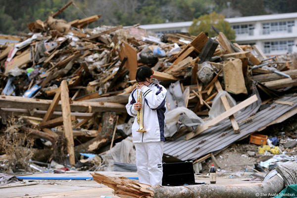 Bức ảnh một cô bé đứng ở một công trường đổ nát đã từng là nhà của cô. Cô đã mất ông bà và mẹ trong vụ động đất. Cô thổi kèn trumpet và nói: 