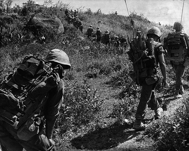 March 1966, Quang Ngai, Vietnam --- U.S. Marines move onto a hill in Quang Ngai Province in March 1966, after it had been secured shortly before by lead elements of the battalion. Battalion radio men are at right. Marine at left shows sign of stress and fatigue. Troops would not have been this bunched up if area had not been secured. Each Marine carries at least two canisters of water.