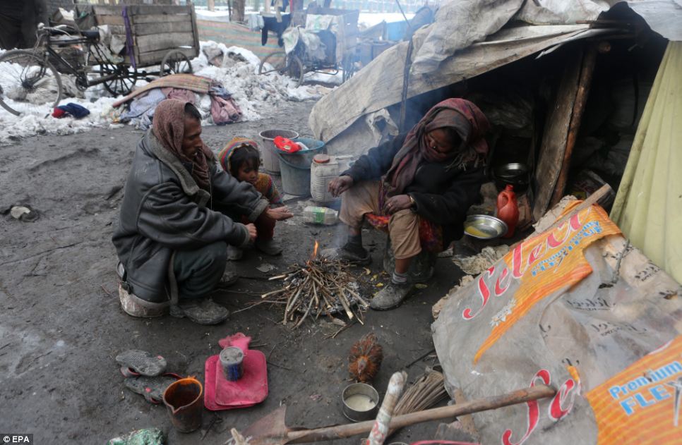 Một gia đình Ấn Độ ấm mình bên ngoài một căn lều tạm được xây dựng từ các tông ở Srinagar, Kashmir trong điều kiện đóng băng hiện nay.  Người đàn ông là một bảng chọn rag, nhặt rác thải thông qua và sau đó cố gắng bán nó