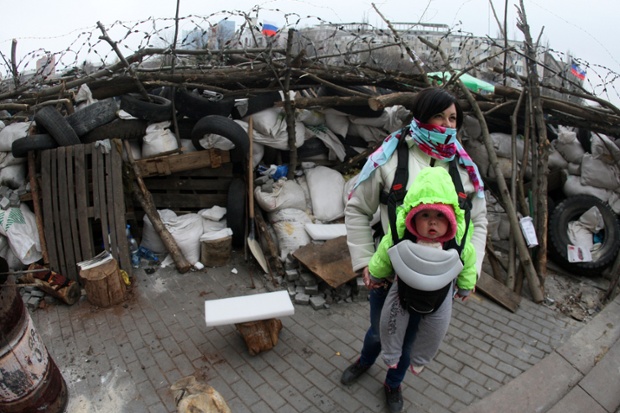 Một phụ nữ bế con đứng trước hàng rào bên ngoài tòa nhà chính quyền ở Donetsk, Ukraine.