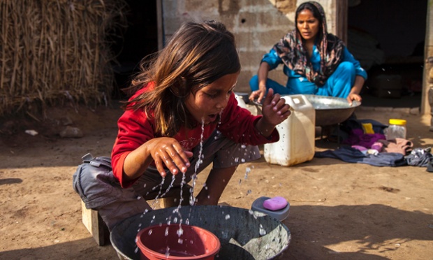 Bé gái rửa mặt trong khi mẹ giặt quần áo tại một khu ổ chuột ở ngoại ô Islamabad, Pakistan.