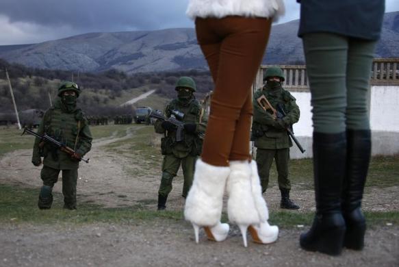 Phụ nữ người địa phương đứng nhìn các binh sĩ được cho thuộc quân đội Nga đứng gác cạnh một căn cứ quân sự của Ukraine ở Perevalnoe.