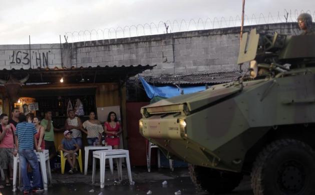 Người dân nhìn các binh sĩ Hải quân Brazil tuần tra bằng xe bọc thép tại khu ổ chuột Mare ở Rio de Janeiro.