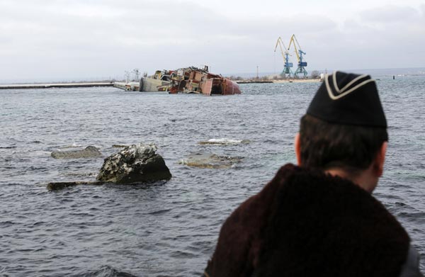 Một thủy thủ Hải quân Nga đang nhìn xác tàu chiến của nước mình chặn cửa ra vào cảng biển ở Crimea.