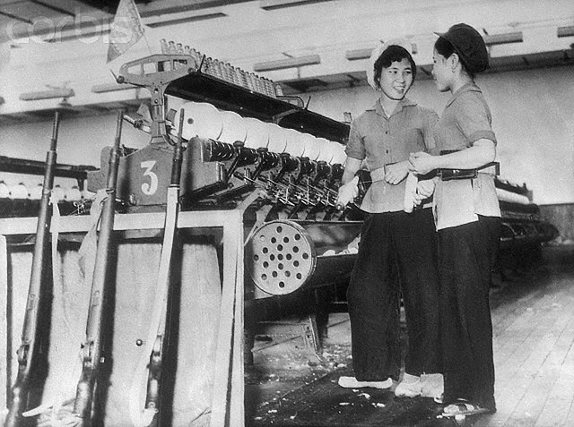 8/14/65-Hanoi, Vietnam: With the stepped up air attacks against targets in North Viet Nam, defense measures have been increased throughout that country. Here, women factory workers in the capital of Hanoi keeep their rifles next to their machine as they go about their jobs. --- Image by © Bettmann/CORBIS